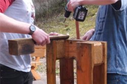 Zwei Schüler bohren mit einer Bohrmaschiene ein Loch ins Holz.